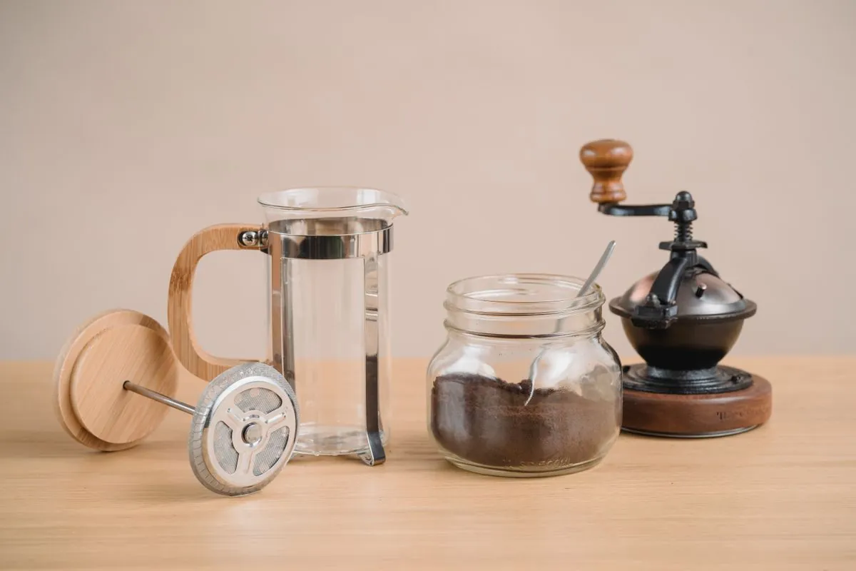 Prensa francesa, café moído e moedor manual sobre a mesa